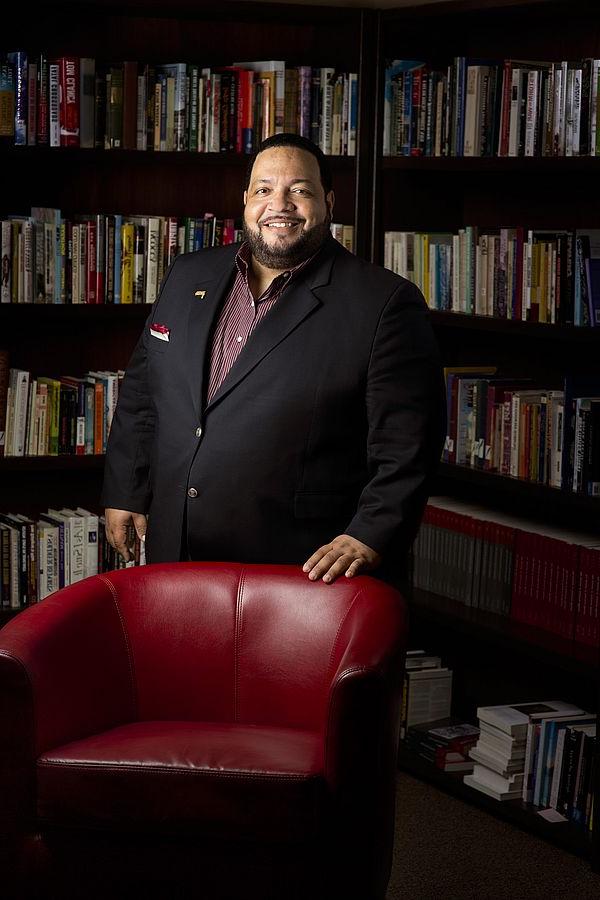 Photo of Tim Golden standing behind a chair in front of books