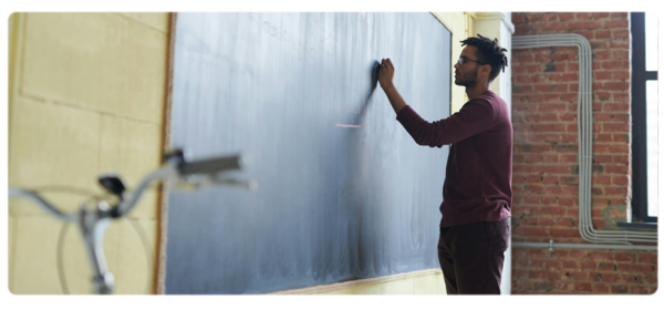 Person stands at blackboard and writes with chalk