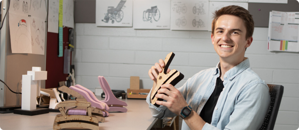 A student proudly presents his product design project to the camera.